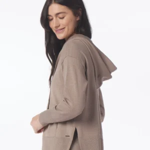 A woman wearing a tan hoodie and black pants.