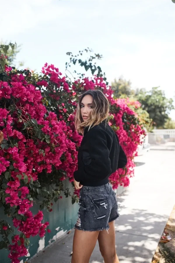 A woman standing next to some flowers on the street.