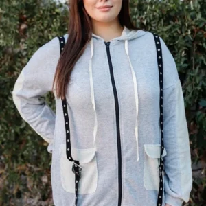 A woman standing in front of a wall wearing a gray hoodie.