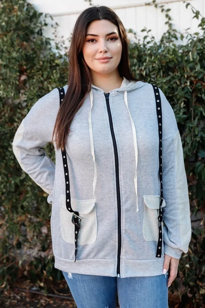 A woman standing in front of a wall wearing a gray hoodie.