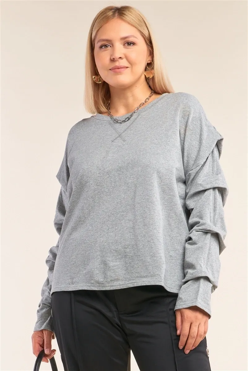 A woman wearing a gray sweatshirt with ruffles on the sleeves.