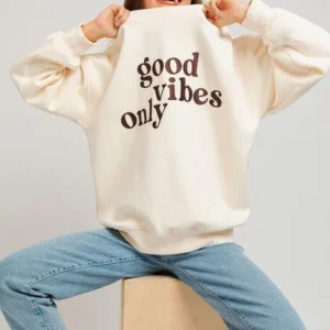 Woman in cream sweatshirt with "good vibes only" text.