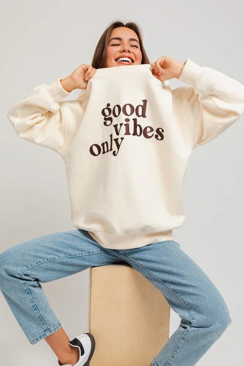 Woman in cream sweatshirt with "good vibes only" text.